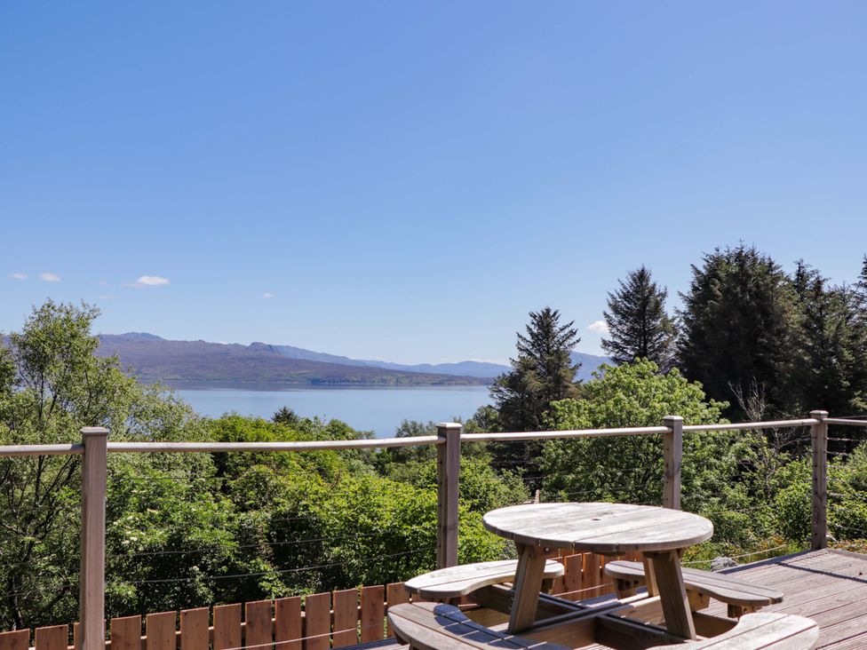 A view from a deck with a table and benches overlooking a river and mountains at The Lookout Saasaig near Broadford