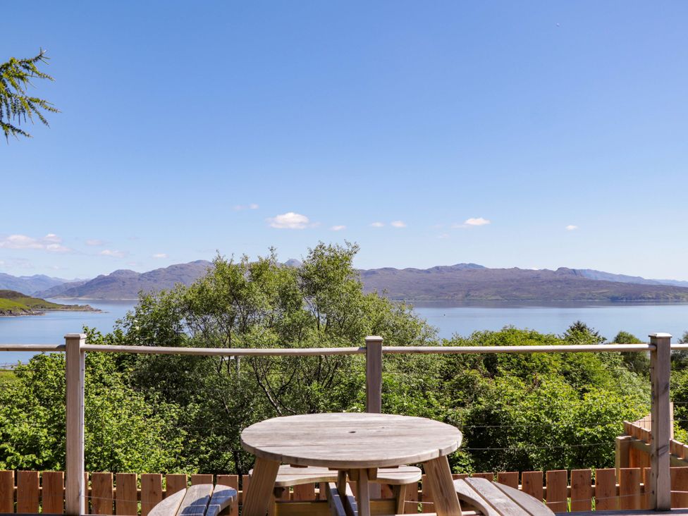 A view from a deck with a table overlooking water and mountains at The Lookout in Saasaig near Broadford