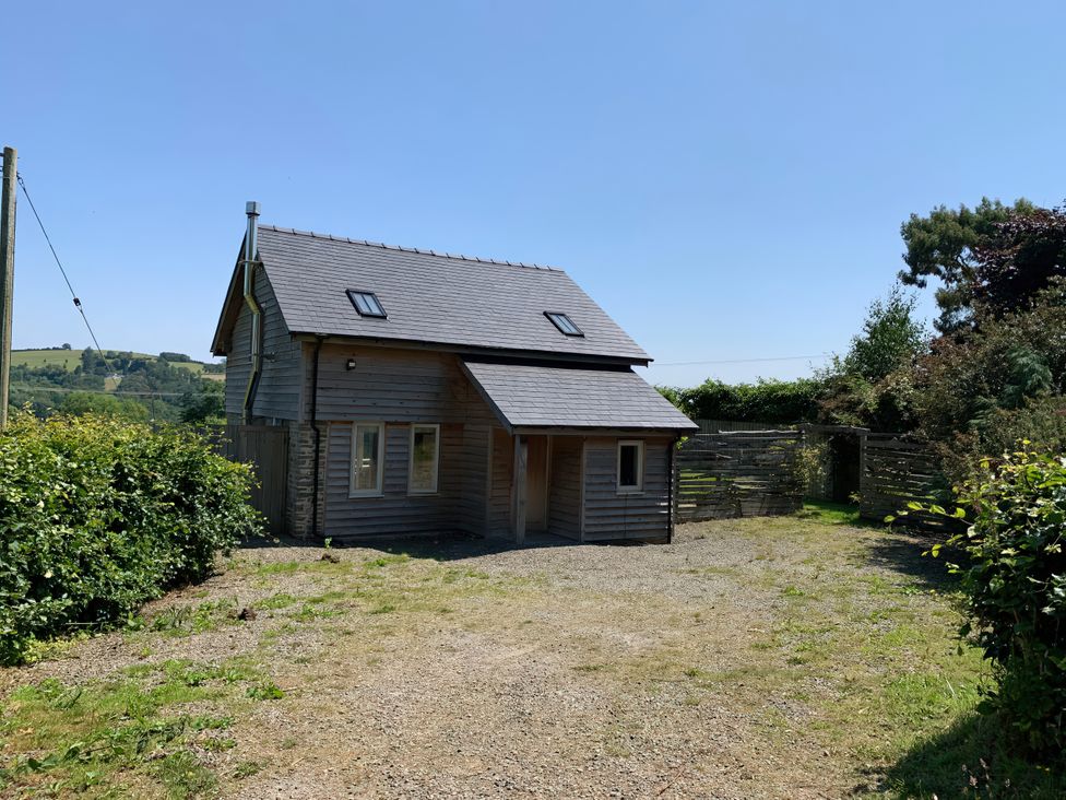 An exterior view of a house with a gravel area and green vegetation at Brynlikky Cottage in Chapel Lawn near Bucknell