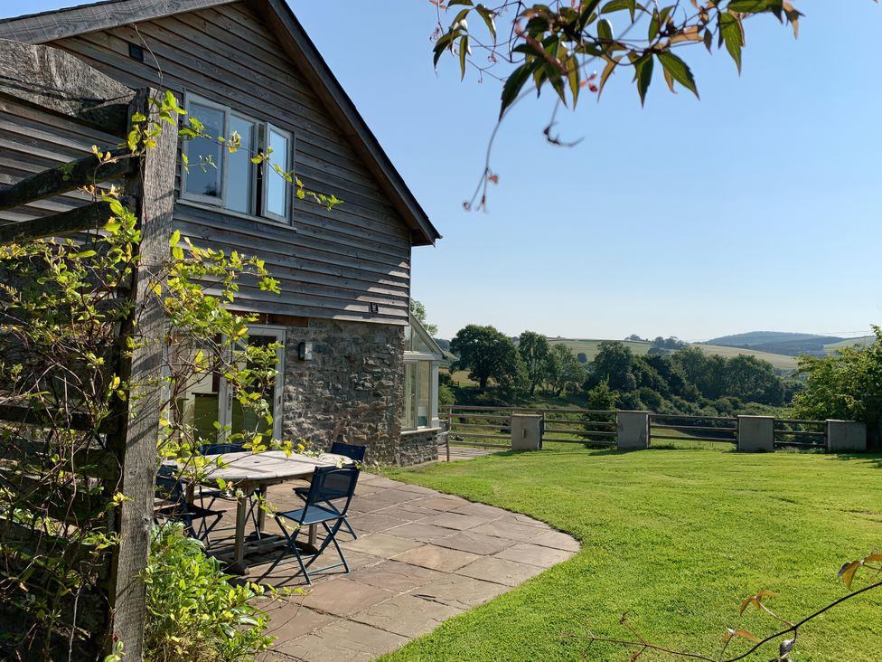 A garden with a stone house and wooden table at Brynlikky Cottage Chapel Lawn near Bucknell