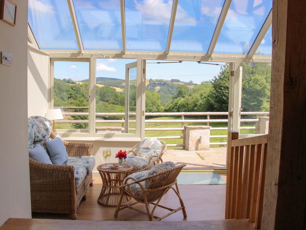 A conservatory with seating area and glass roof at Brynlikky Cottage Chapel Lawn near Bucknell