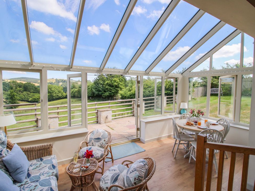 A conservatory with a table and chairs at Brynlikky Cottage in Chapel Lawn near Bucknell