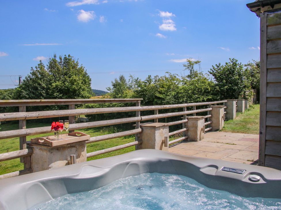 An outdoor area with a hot tub and a table with flowers at Brynlikky Cottage Chapel Lawn near Bucknell
