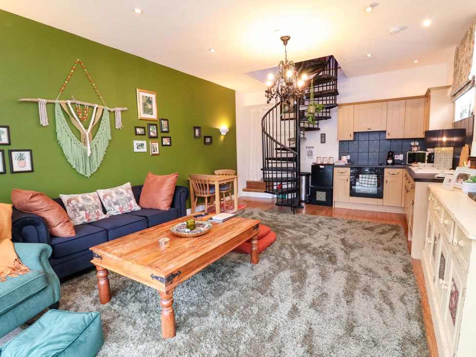 A living room with a spiral staircase and kitchen units at The Coach House, The Grove in Combe Martin