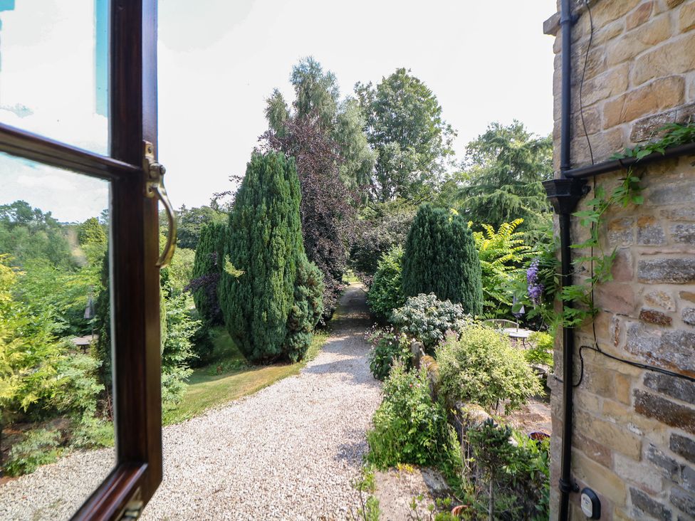 A view of a garden with a gravel path and trees at Green Farm Cottage in Hognaston near Carsington Water