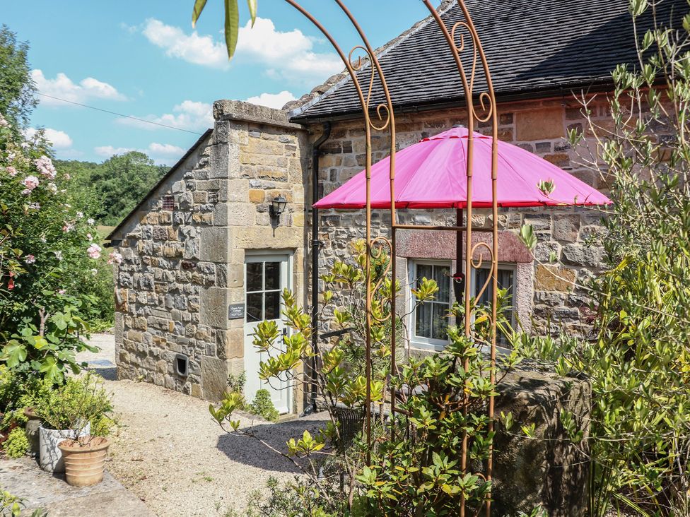 A garden area with a stone wall and a pink umbrella at Green Farm Cottage Hognaston near Carsington Water