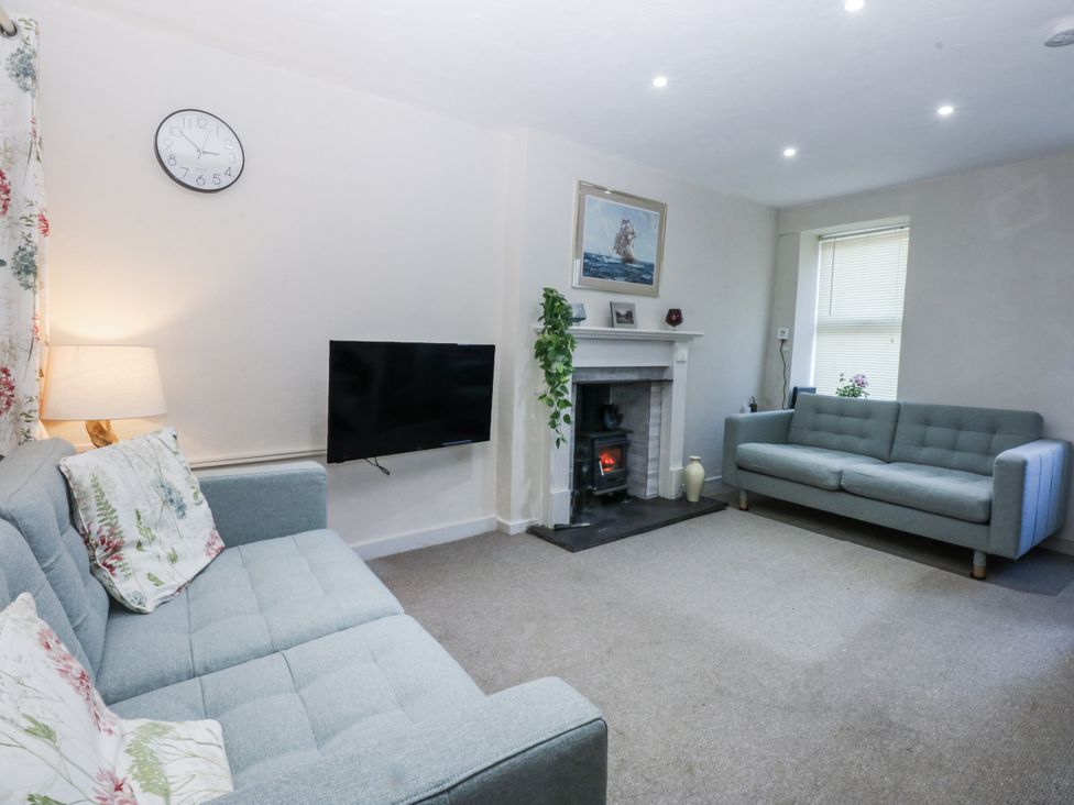 A living room with a clock, two sofas, a television, and a fireplace at 3 Tyn Giat in Penysarn near Amlwch