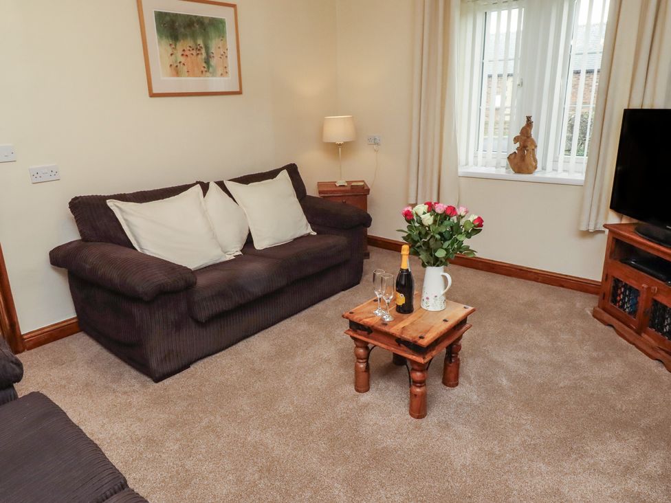 A living room with a sofa, coffee table, flowers, and a TV at The Retreat in Embleton