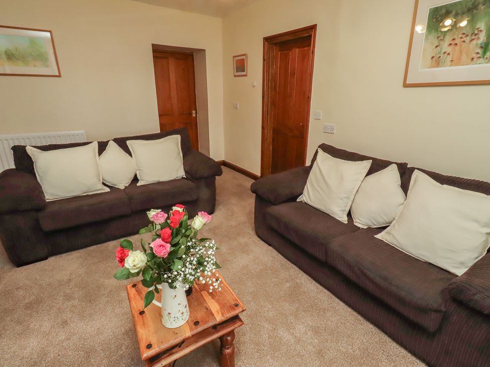 A living room with two sofas and a table with flowers at The Retreat in Embleton