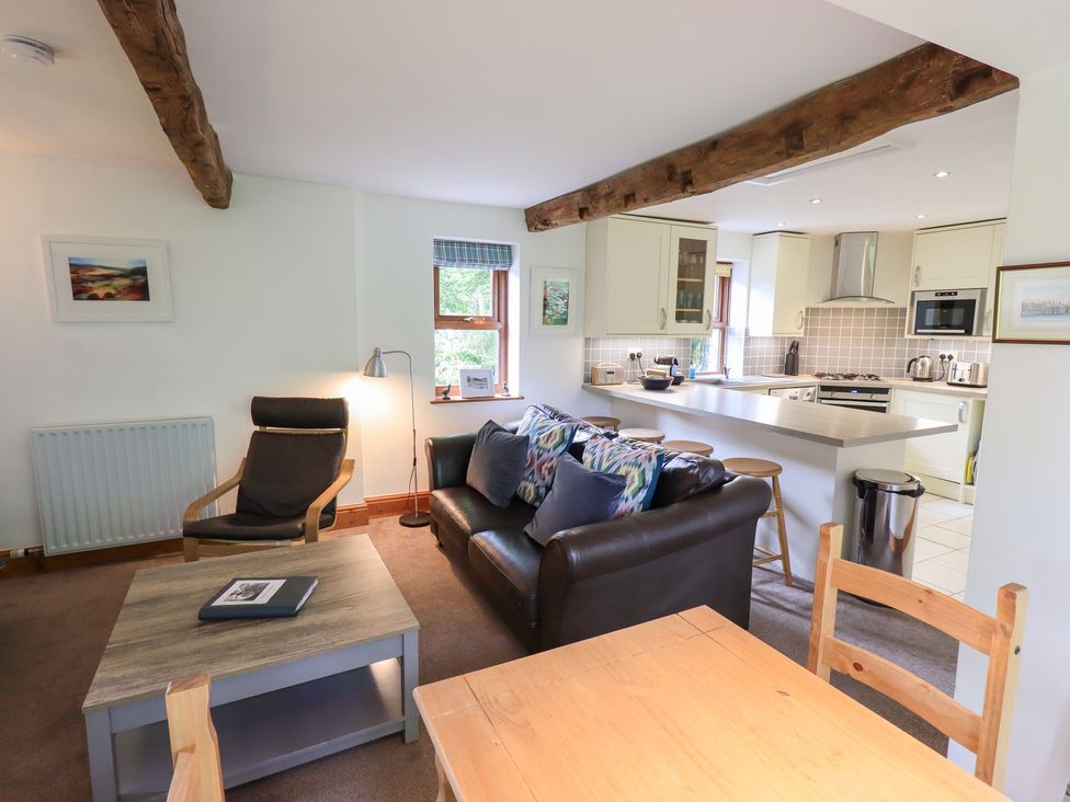 A living room with kitchen features a sofa and dining table at Drystones in Grasmere