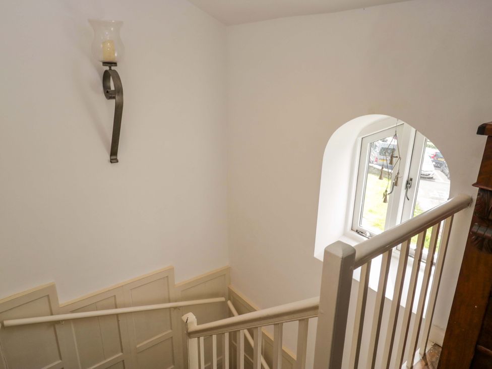 A staircase with a wall sconce and a window at Chapel How, Ambleside