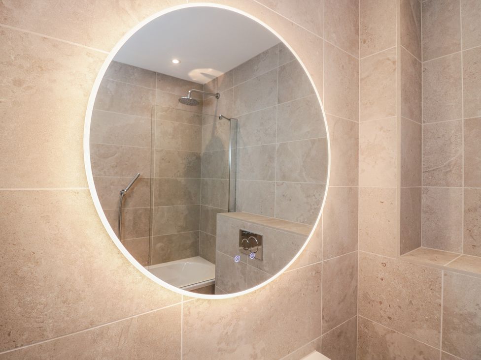 A bathroom with a round mirror and shower at Chapel How in Ambleside