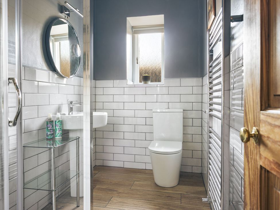 A bathroom with a shower, toilet, sink, and mirror at Herdwick Cottage Ambleside