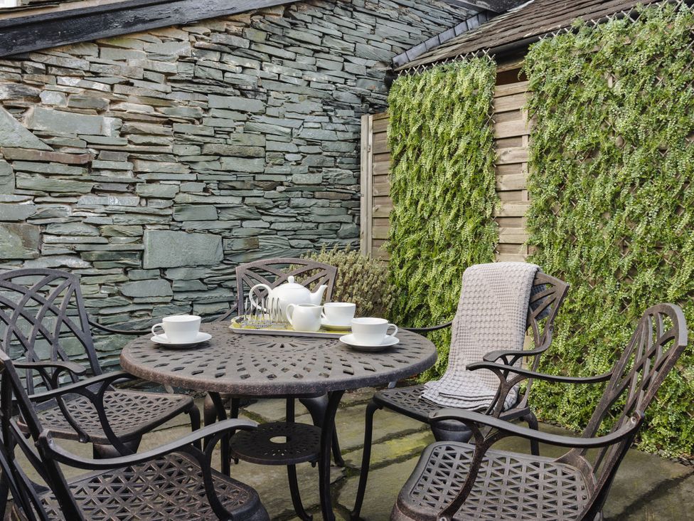 A garden with a stone wall and table set with teapot and cups at Herdwick Cottage Ambleside