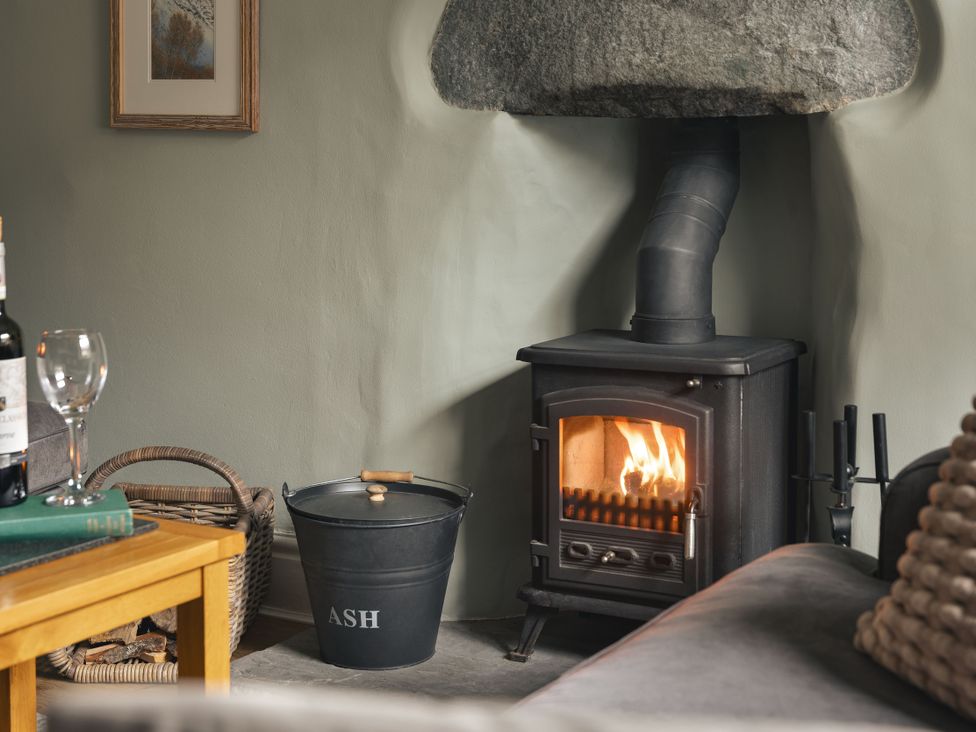 A living room with a wood-burning stove and wine bottle at Herdwick Cottage Ambleside