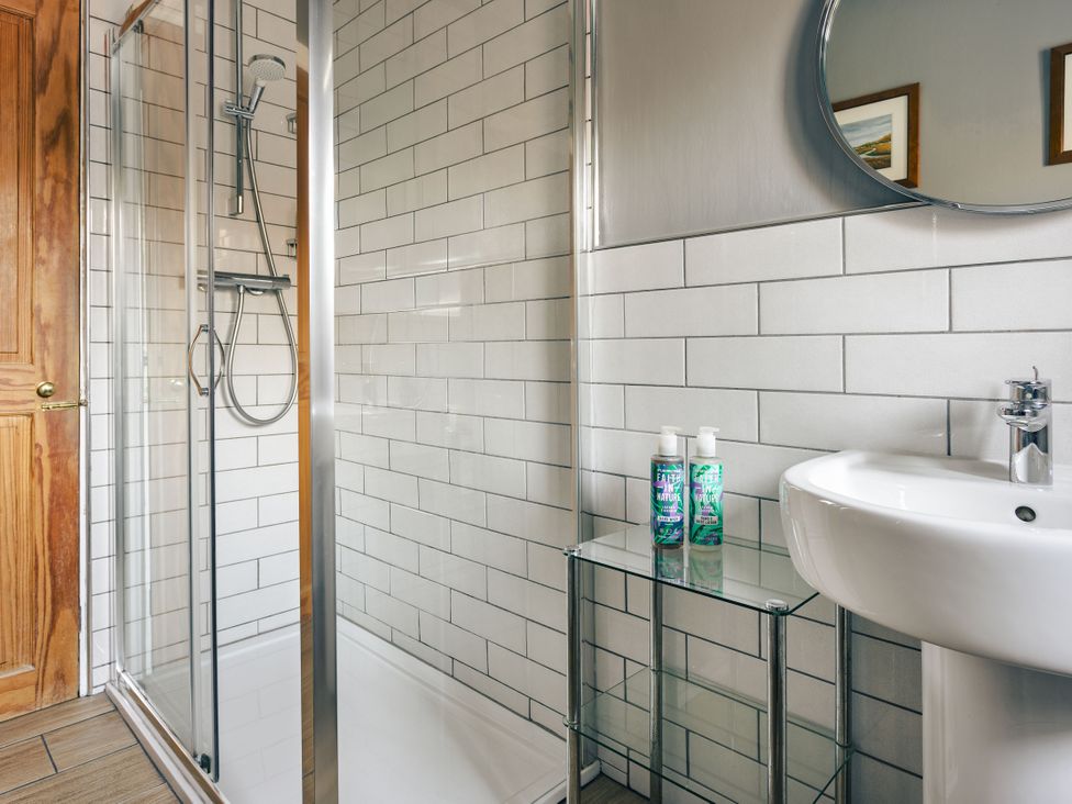 A bathroom with a shower, sink, and mirror at Herdwick Cottage Ambleside