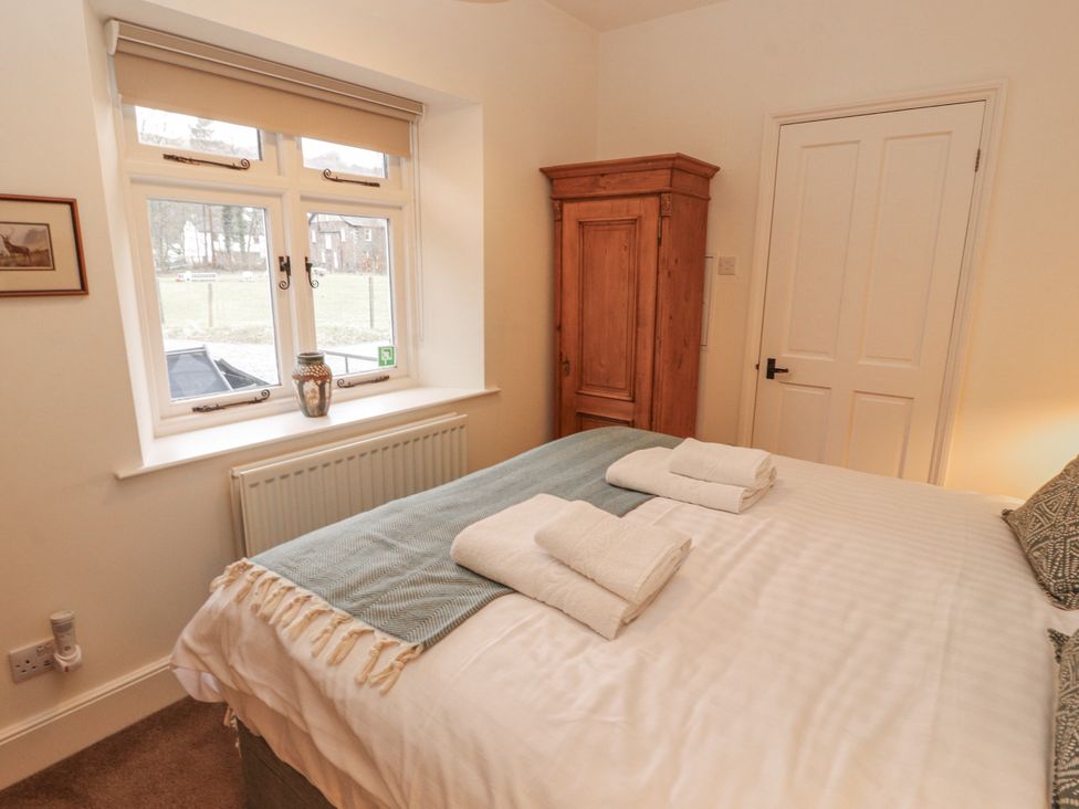 A bedroom with a bed towels on top and a wardrobe at Rowan Cottage in Grasmere