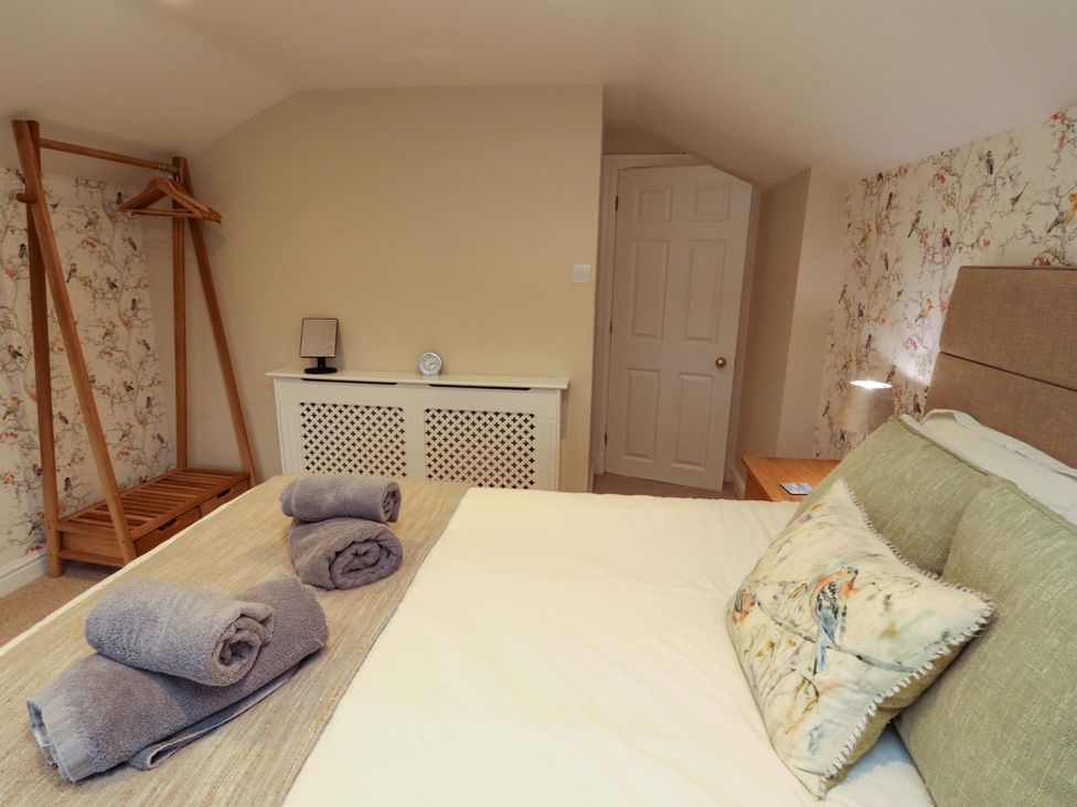 A bedroom with a bed, towels, and a clothes rack at Cragfell Cottage in Cartmel Fell