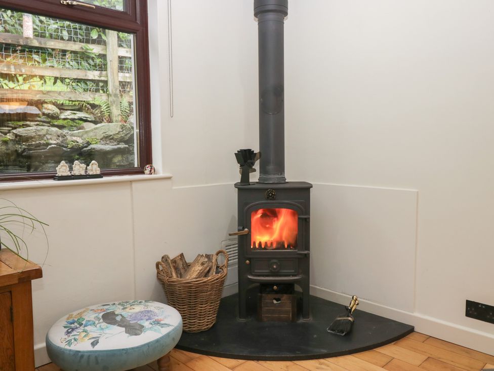 A living room with a wood stove and logs at Corner Cottage in Troutbeck
