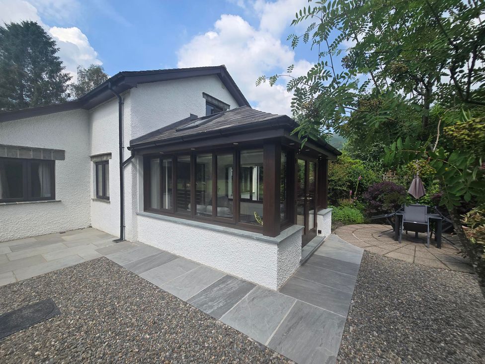 A garden with a conservatory and outdoor seating at Rowanberry Cottage in Grasmere