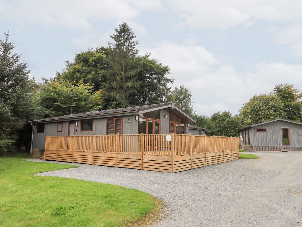 A wooden lodge with a deck and trees at The Loghey in Hawkshead