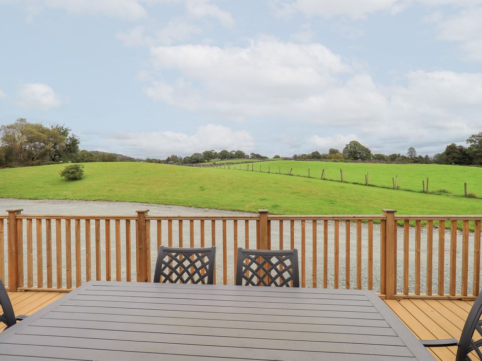 An outdoor area with a wooden table and chairs overlooking grassland at The Loghey in Hawkshead