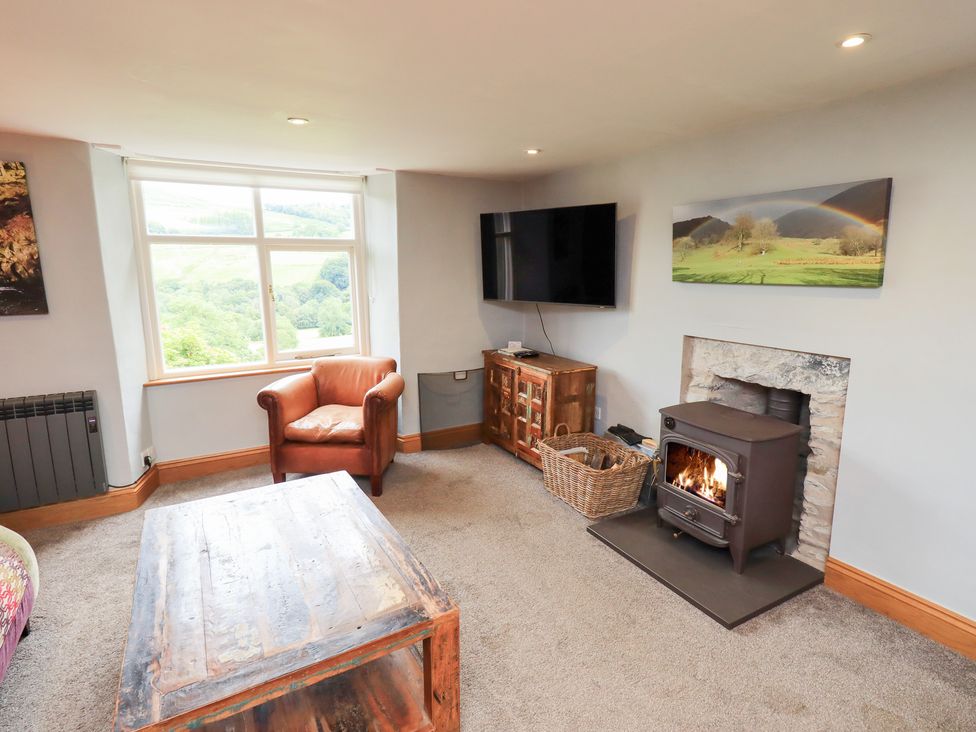 A living room with a wood stove and television at Boxwood Cottage in Troutbeck