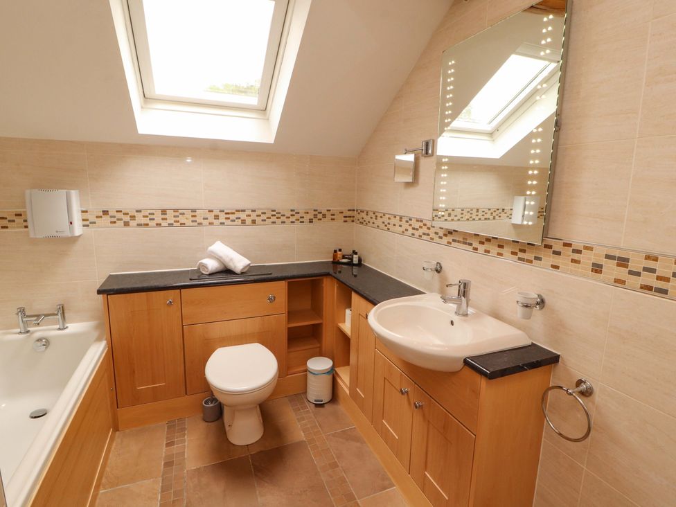 A bathroom with a bathtub, toilet, sink and mirror at Durham Bridge Barn in Crosthwaite