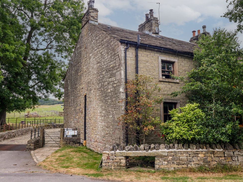 A stone house with a gate and trees at Bay Horse Cottage in Skipton