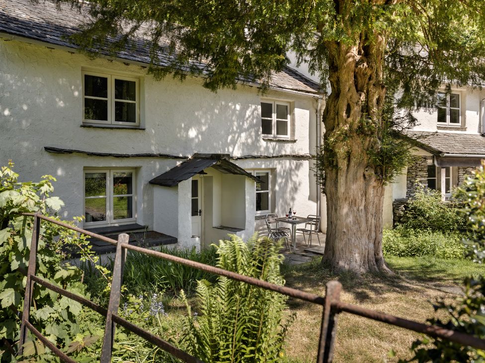 The exterior of a white building with windows a small porch a large tree and a table with two chairs on a patio at High Lindeth in Bowness