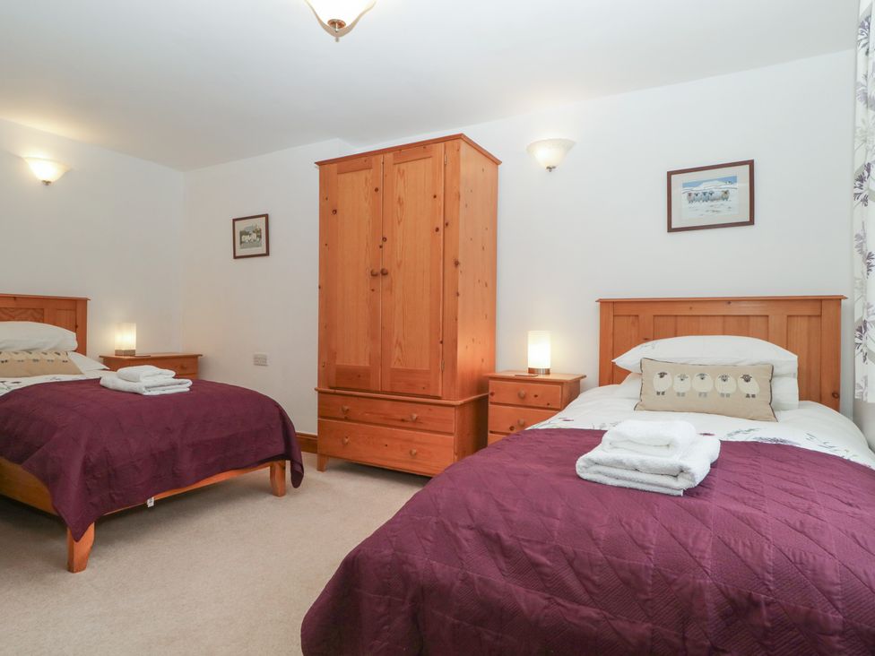 A bedroom with two beds and a wardrobe at Cygnet Cottage Thornthwaite