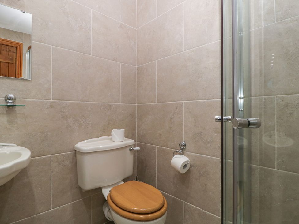 A bathroom with a toilet, sink, shower and mirror at Cygnet Cottage in Thornthwaite