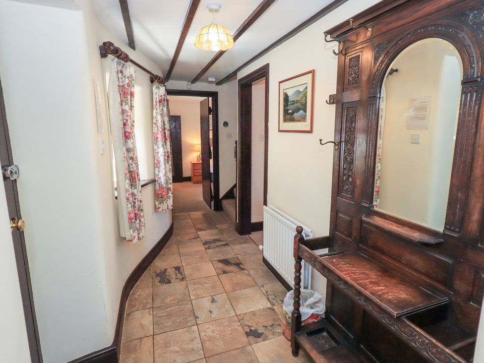 A hallway with tiled floor floral curtains on windows a wooden coat rack with a mirror and an open door leading to another room at The Cottage in Keswick