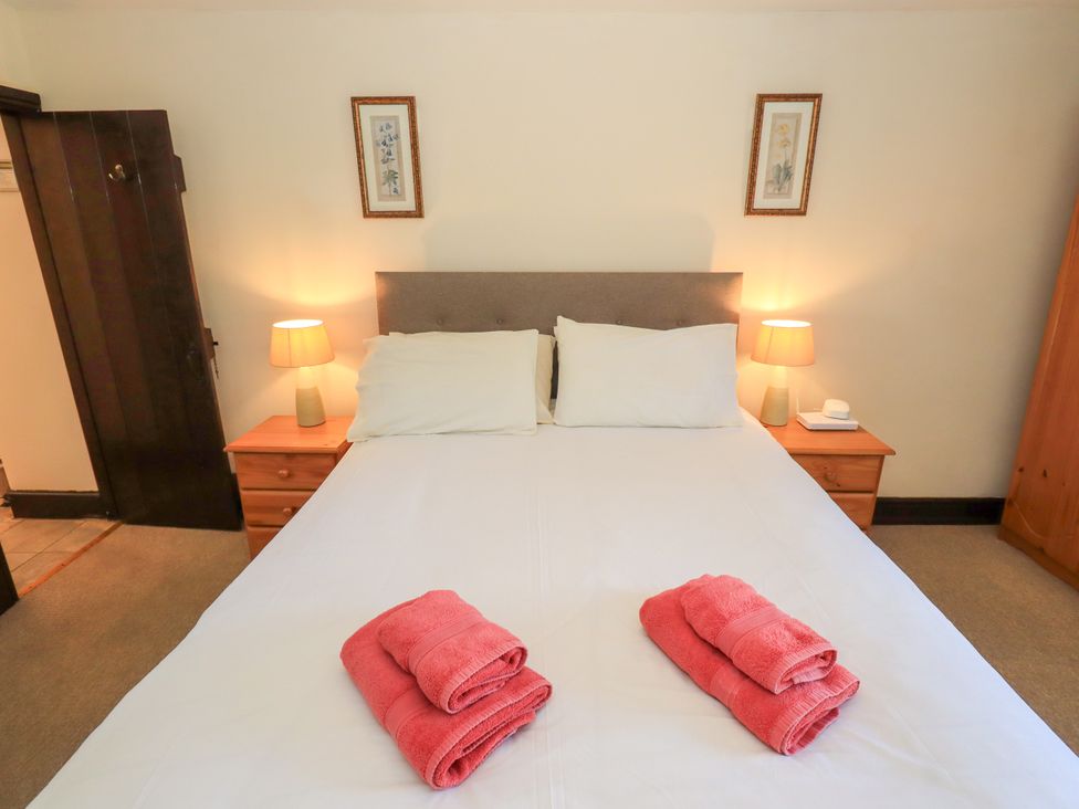 A bedroom with a double bed with white bedding and pink towels on top two bedside tables with lamps and framed artwork on the wall at The Cottage in Keswick