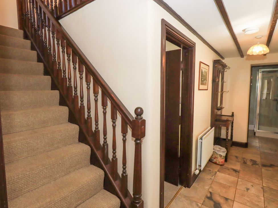 A hallway with carpeted stairs wooden banister a radiator and a wooden coat rack at The Cottage in Keswick