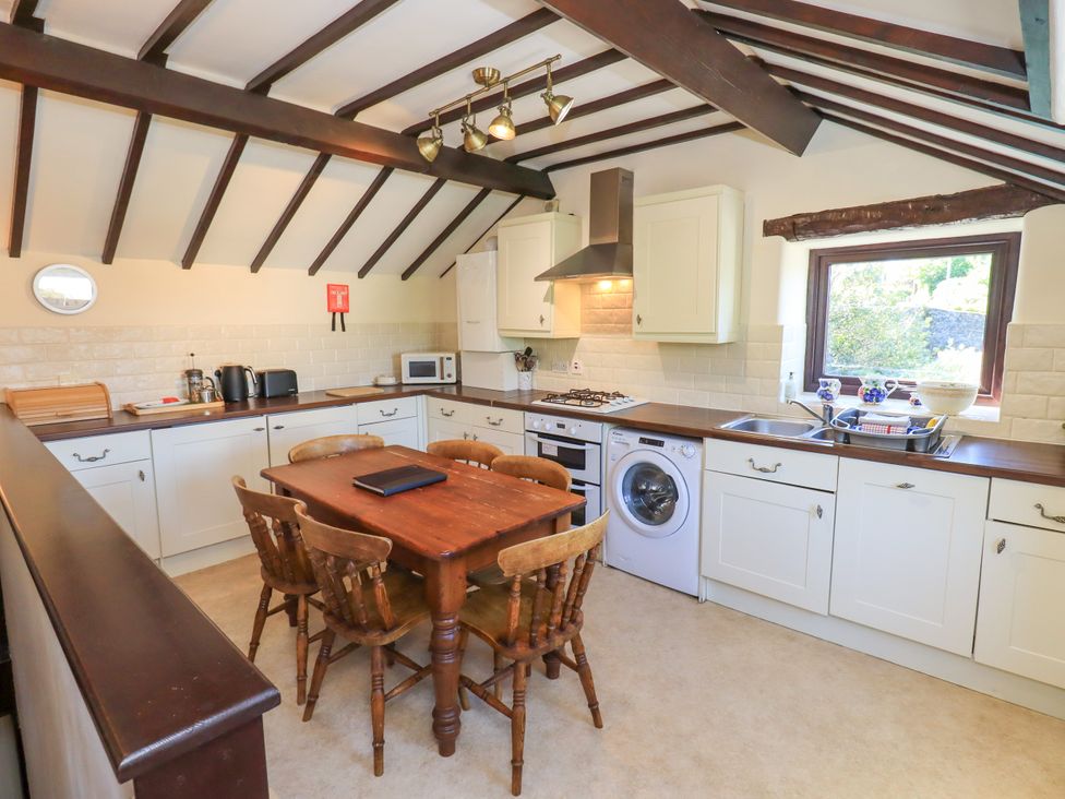 A kitchen with wooden ceiling beams wooden table and chairs white cabinets and appliances at The Cottage in Keswick