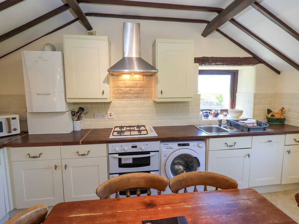 A kitchen with white cabinets a gas stove oven washing machine microwave and wooden dining table at The Cottage in Keswick
