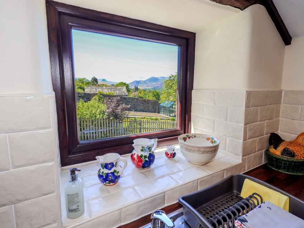 A kitchen window with ceramic pitchers and a bowl on the sill and a dish rack by the sink at The Cottage in Keswick