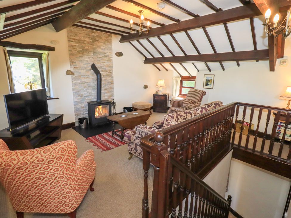 A sitting room with wooden ceiling beams a fireplace and patterned armchairs at The Cottage in Keswick