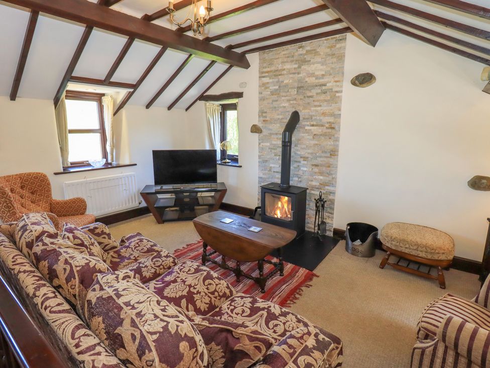 A living room with patterned sofas a wood stove and a television at The Cottage in Keswick