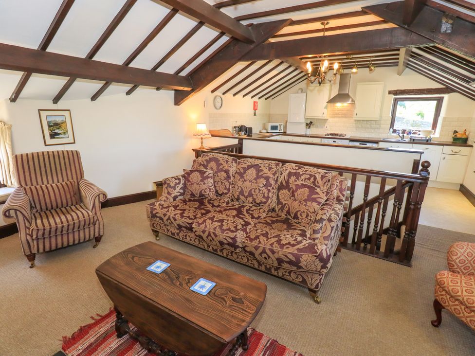 A living room with a patterned sofa armchair and wooden coffee table next to an open kitchen area at The Cottage in Keswick