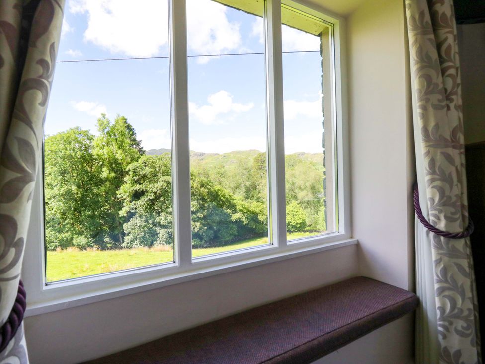 A window with curtains overlooking a green landscape at Elterwater Lodge in Elterwater