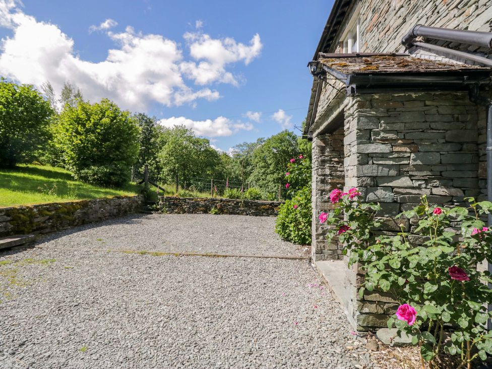 A stone house with a gravel driveway and flowers at Elterwater Lodge in Elterwater