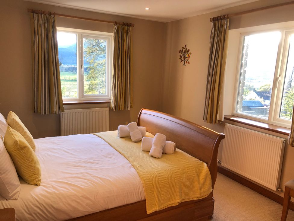 A bedroom with a bed and windows at Dancing Beck Cottage in Millbeck