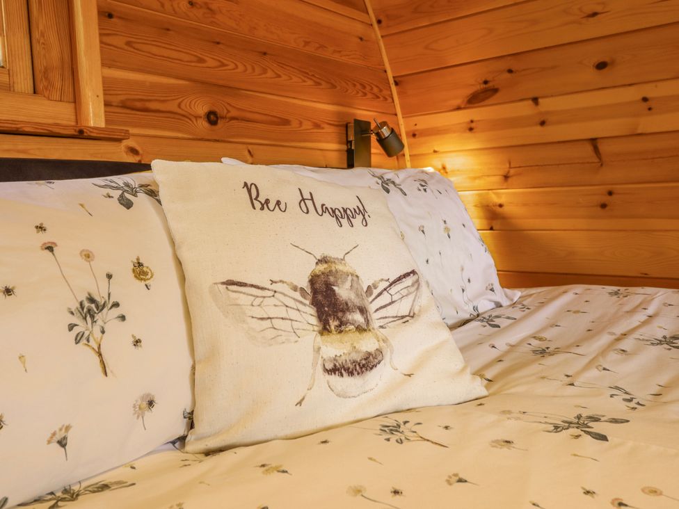 A bedroom with floral bedding and a bee motif pillow at The Rhiw in Llanfair Caereinion