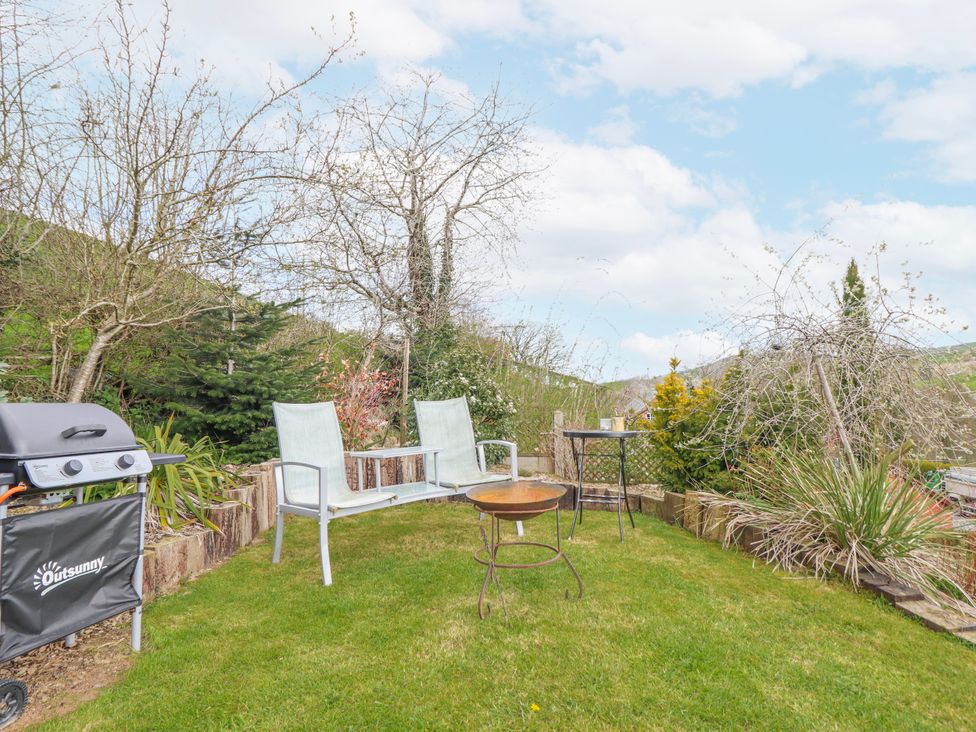 A garden with a barbecue, chairs, and a table at The Rhiw in Llanfair Caereinion