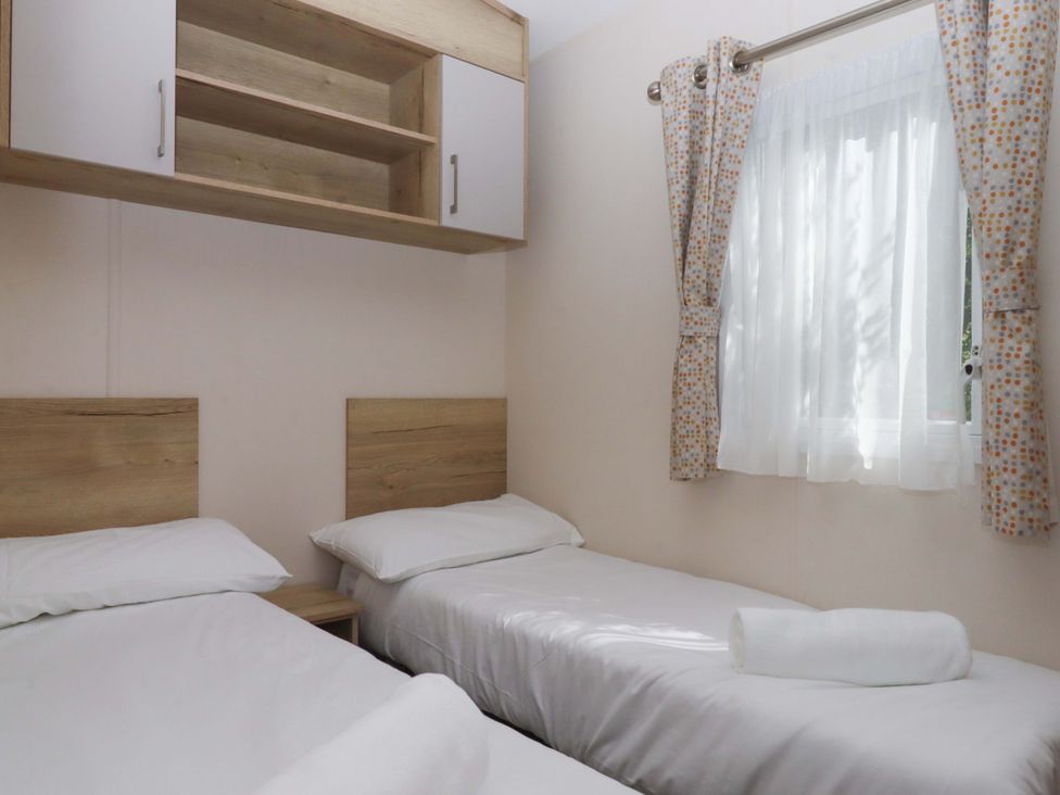 A bedroom with two single beds and a window with curtains at 213 Seaview Caravan 