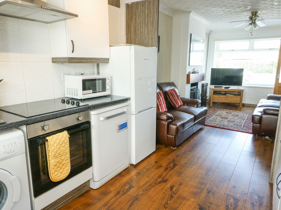 A kitchen with appliances and a living area at Fern Hill Cottage Newborough