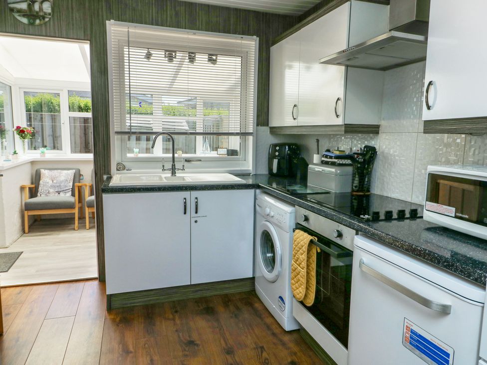 A kitchen with a sink, oven, and washing machine at Fern Hill Cottage in Newborough