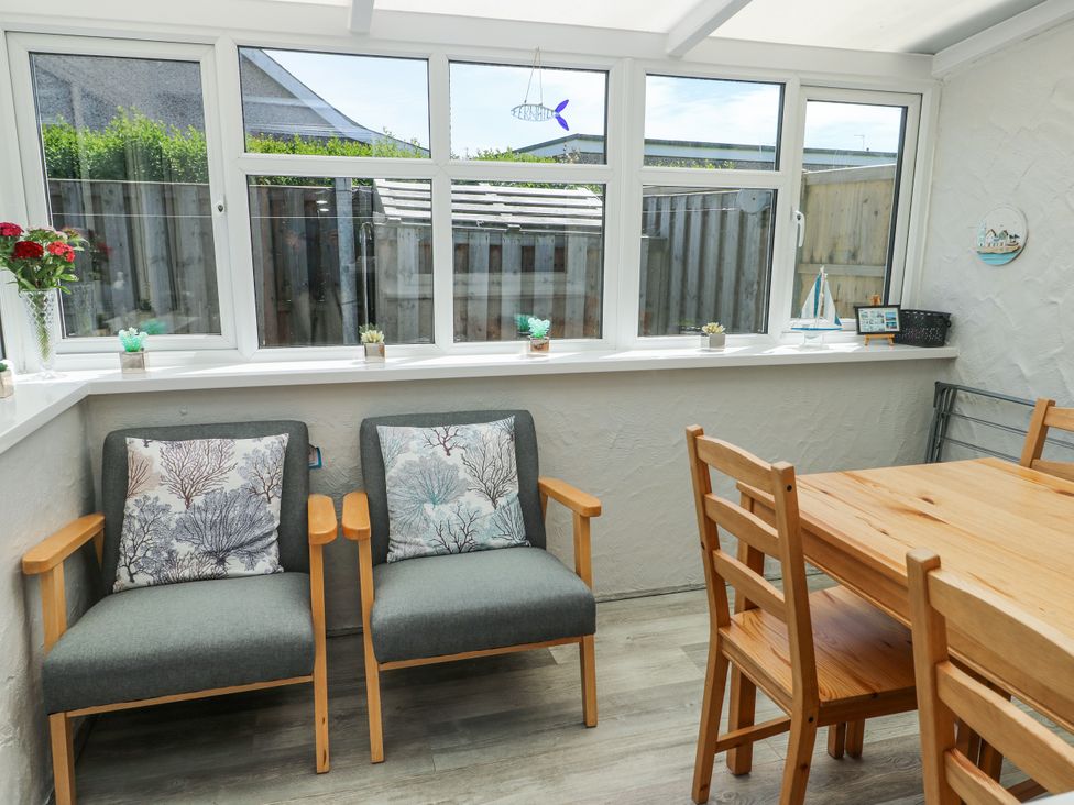 A conservatory with chairs and dining table at Fern Hill Cottage in Newborough